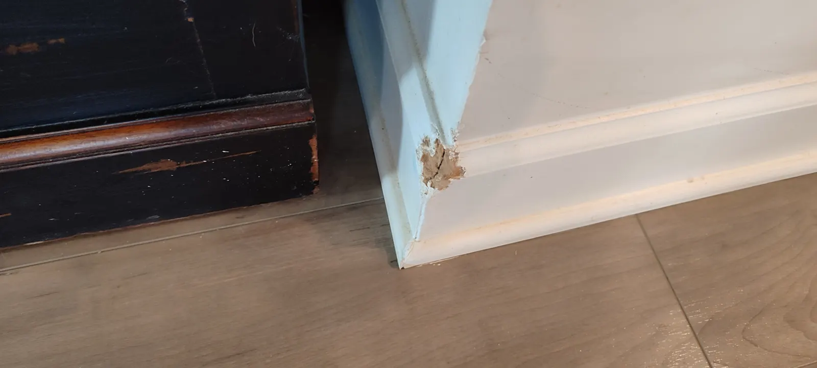 Chipped baseboard corner beside a dark cabinet