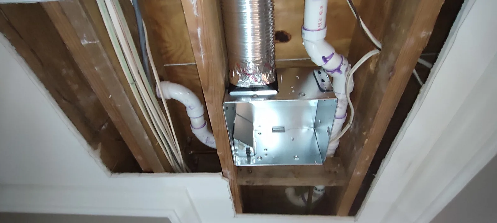 Exhaust fan and light housing positioned between ceiling framing before the drywall repair