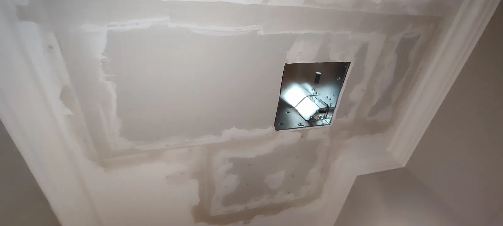 New drywall installed around the bathroom exhaust fan opening during ceiling restoration