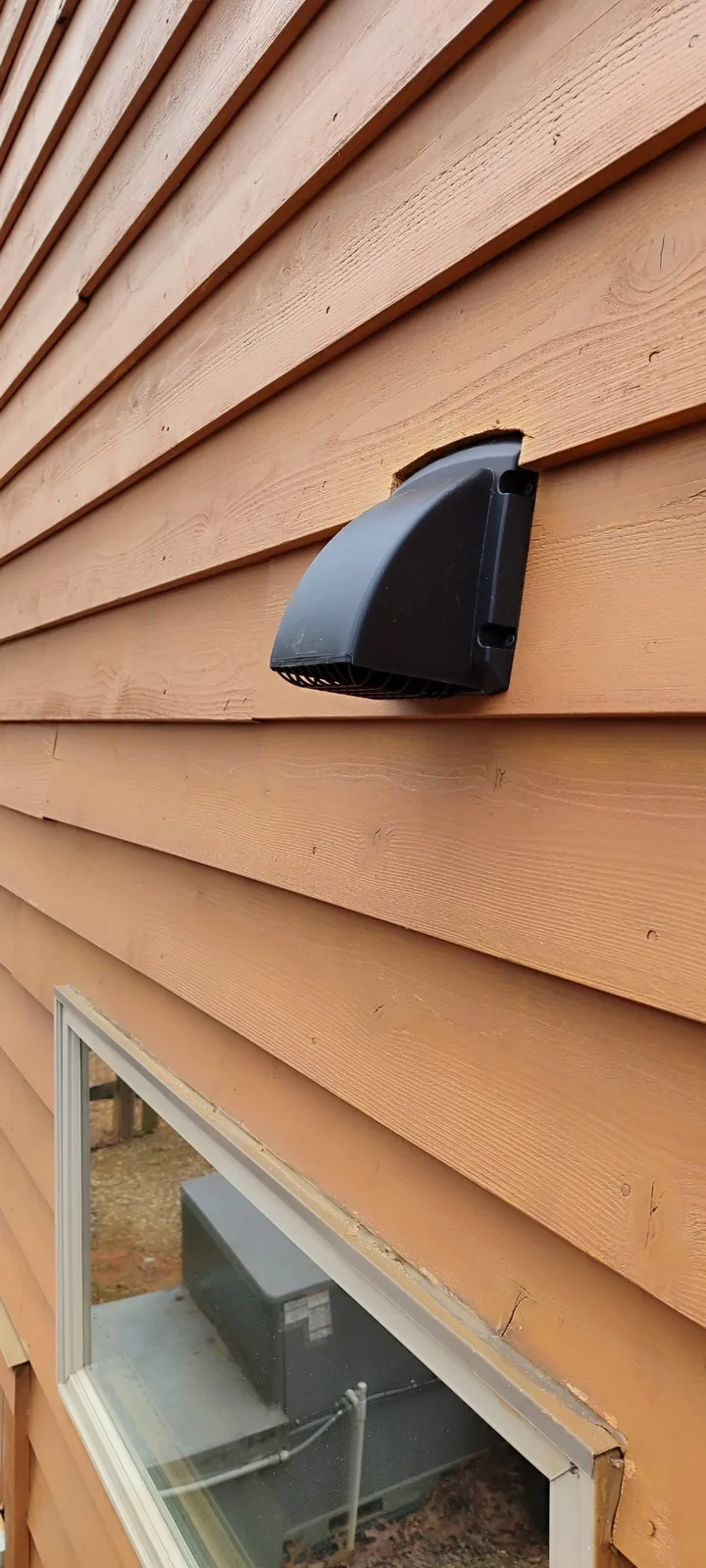 New exterior bathroom exhaust vent hood installed on wood siding above a window