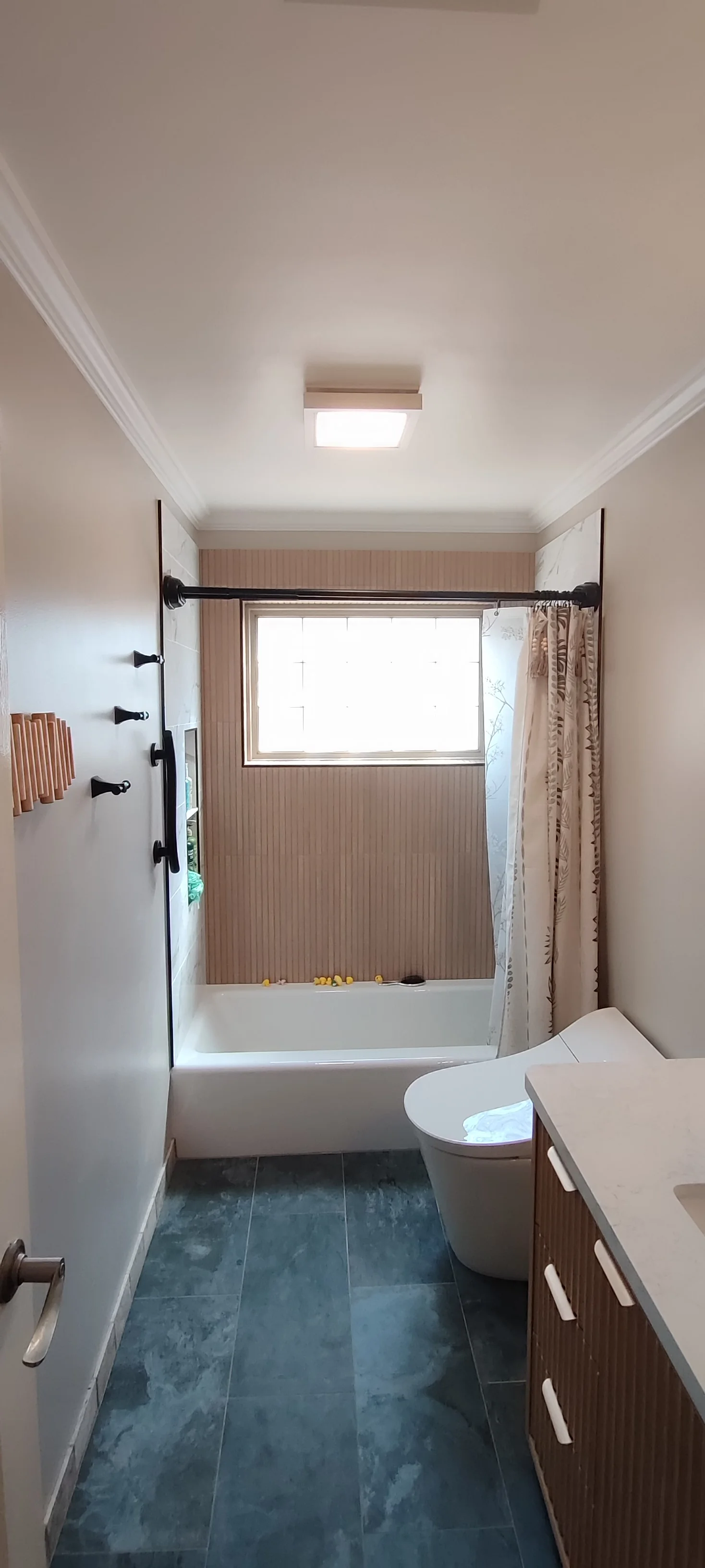 Completed bathroom viewed from the doorway, with dark floor tiles and a tiled bath surround.