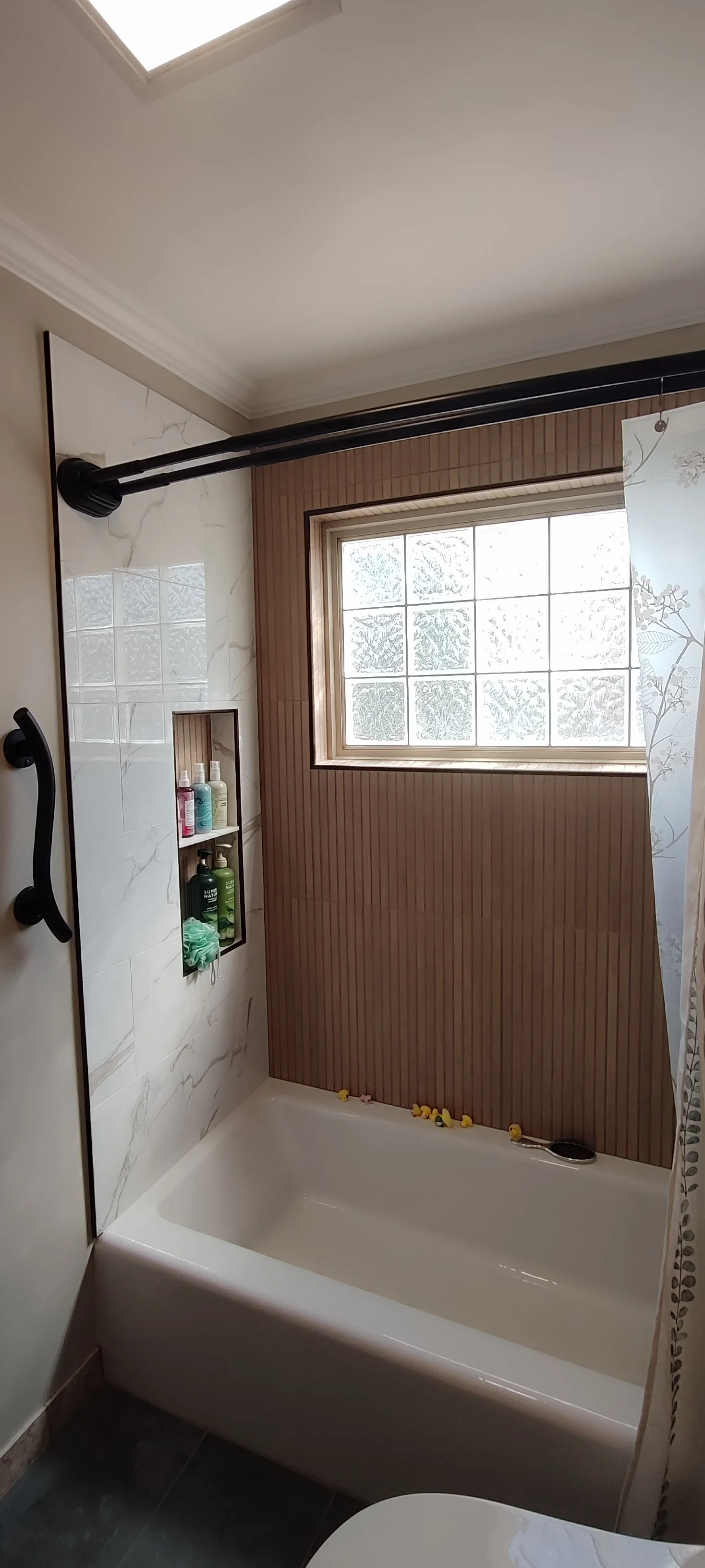 Left side of the completed bath surround, with a recessed niche and black fittings. Toiletries remain visible in the niche.