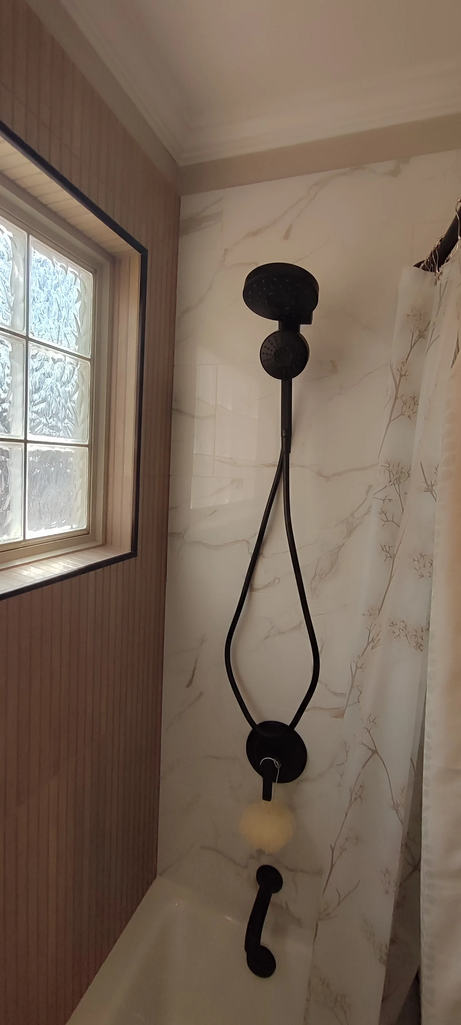 Marble-look wall tiles and black shower fittings beside the glass-block window.