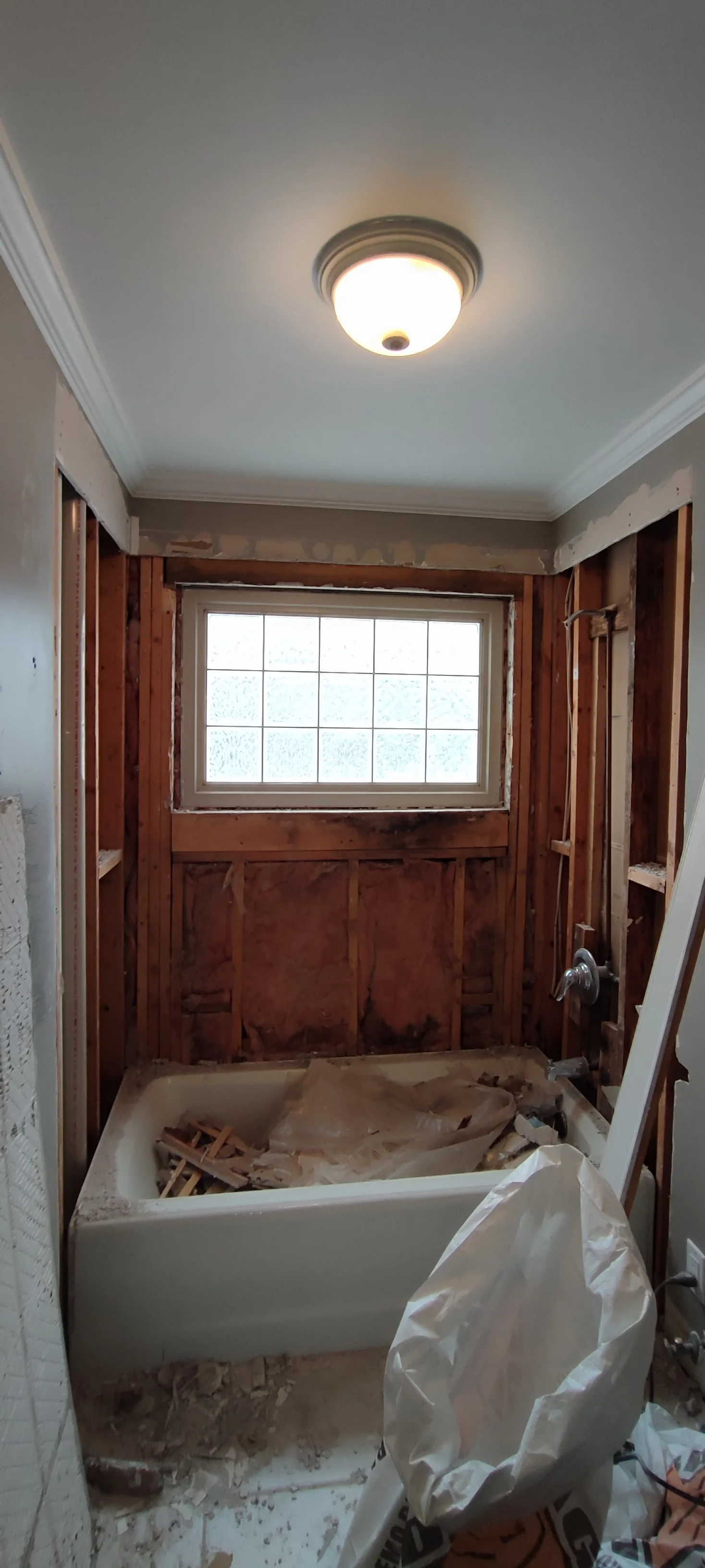 Bath surround during demolition, with exposed framing and the tub covered for the work.