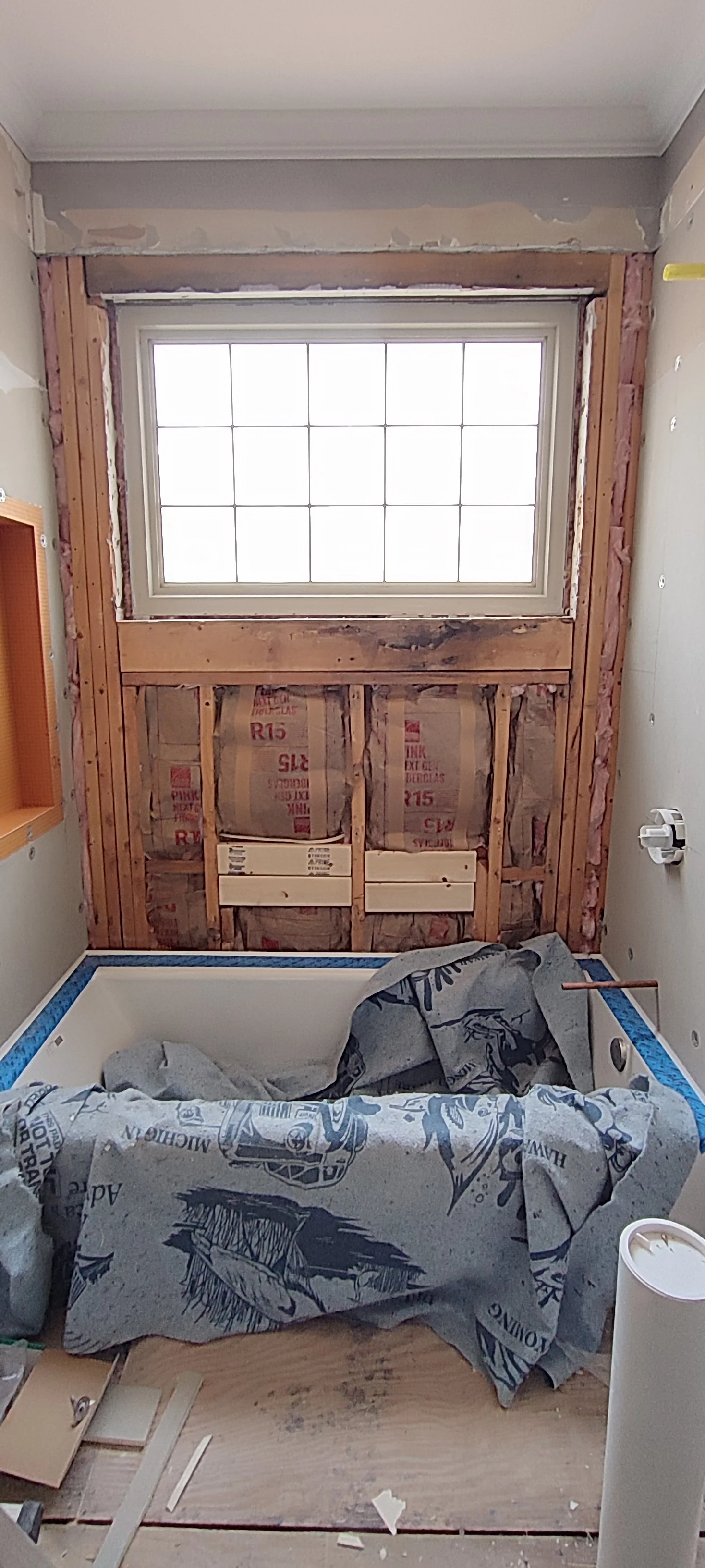 Wall boarding in progress around the bathtub, with framing still visible beneath the window.