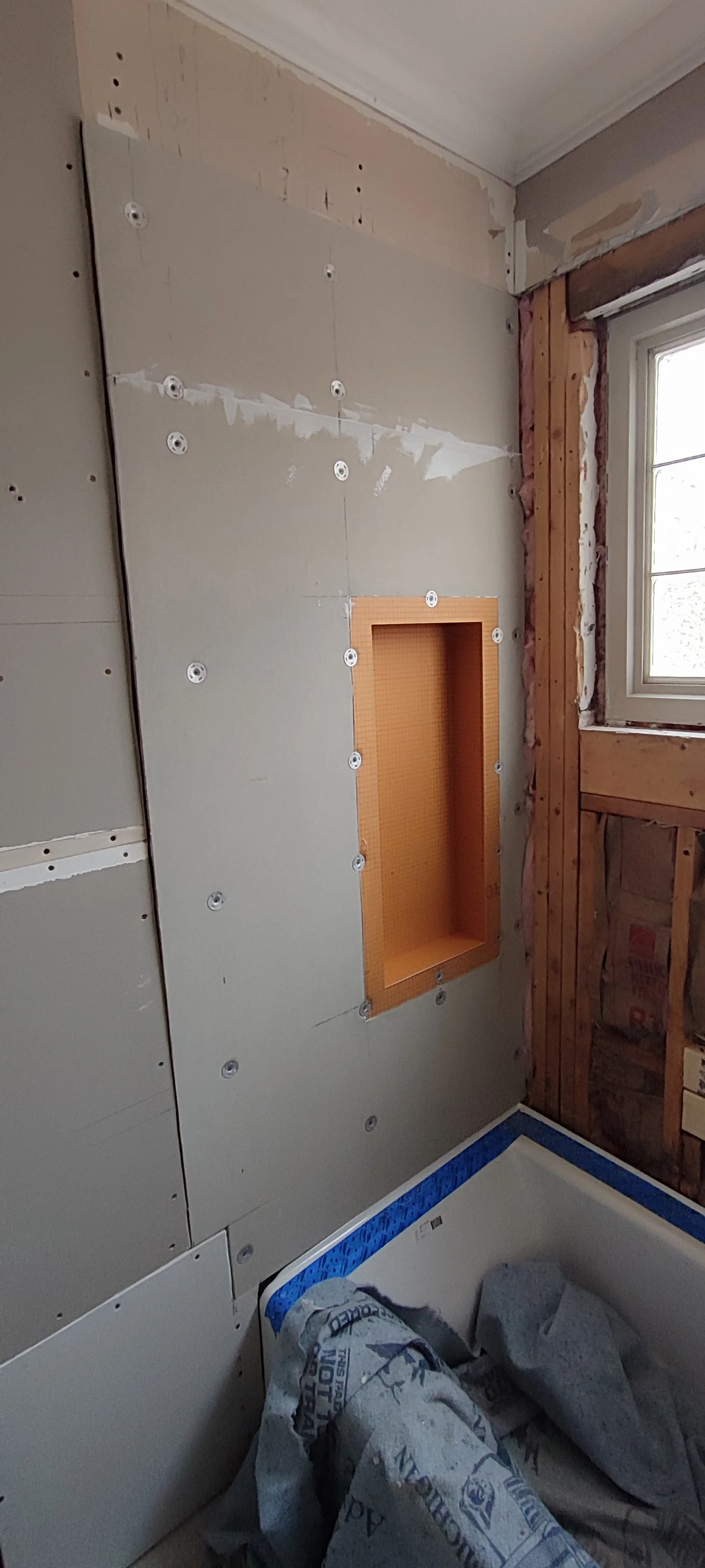 Recessed niche and wall boards before tiling on the left side of the bathtub.