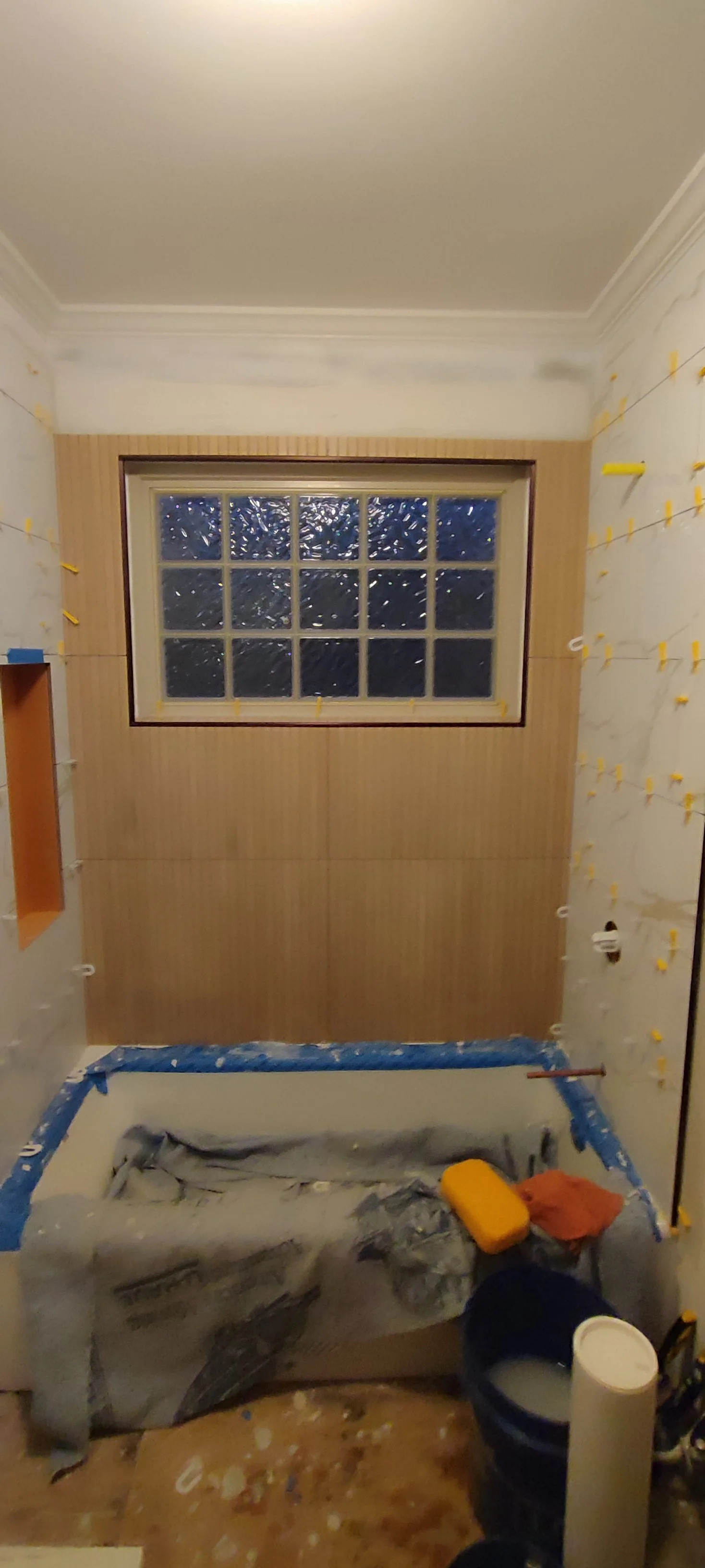 View of the bath surround during tiling, with tools and protective covering still in the work area.