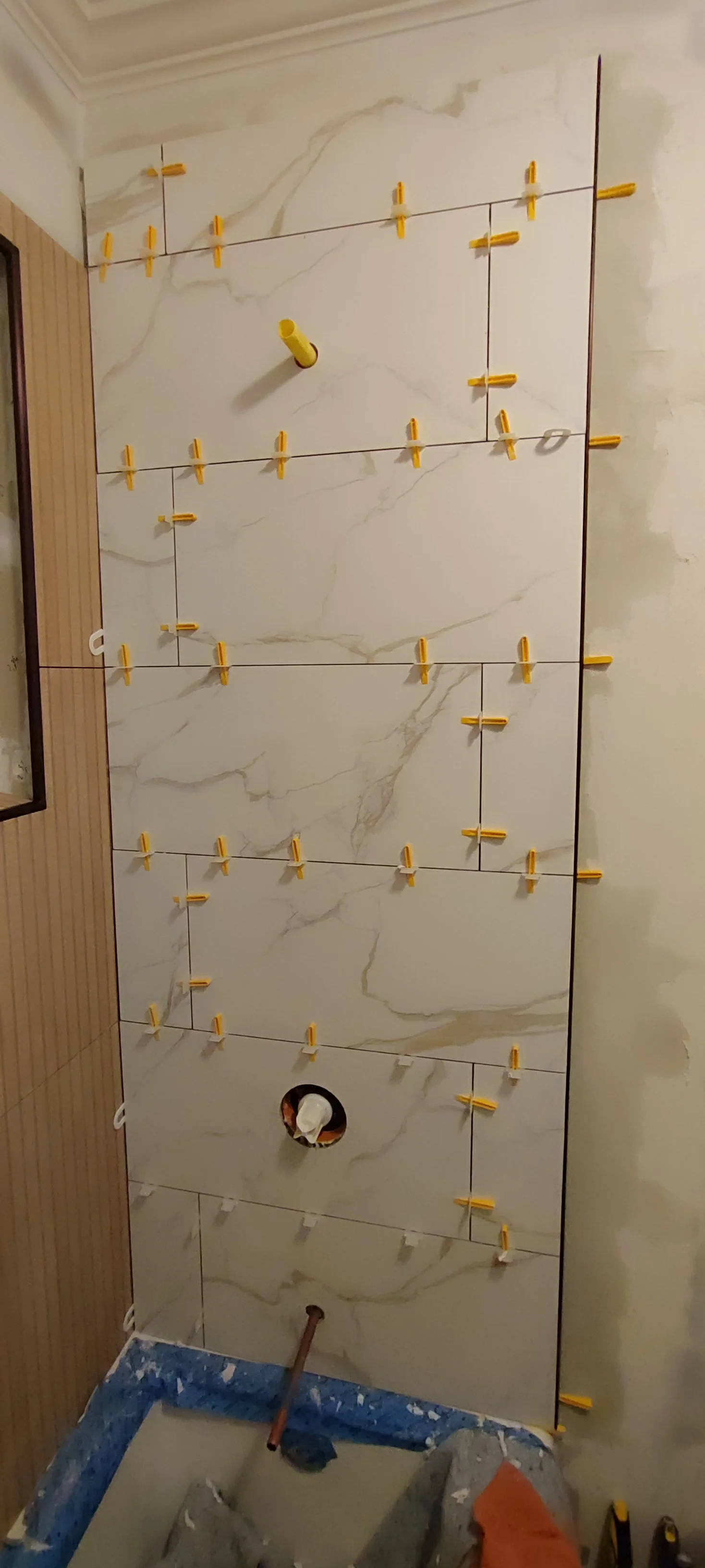 Shower wall tiles during installation, with clips and unfinished fixture openings visible.