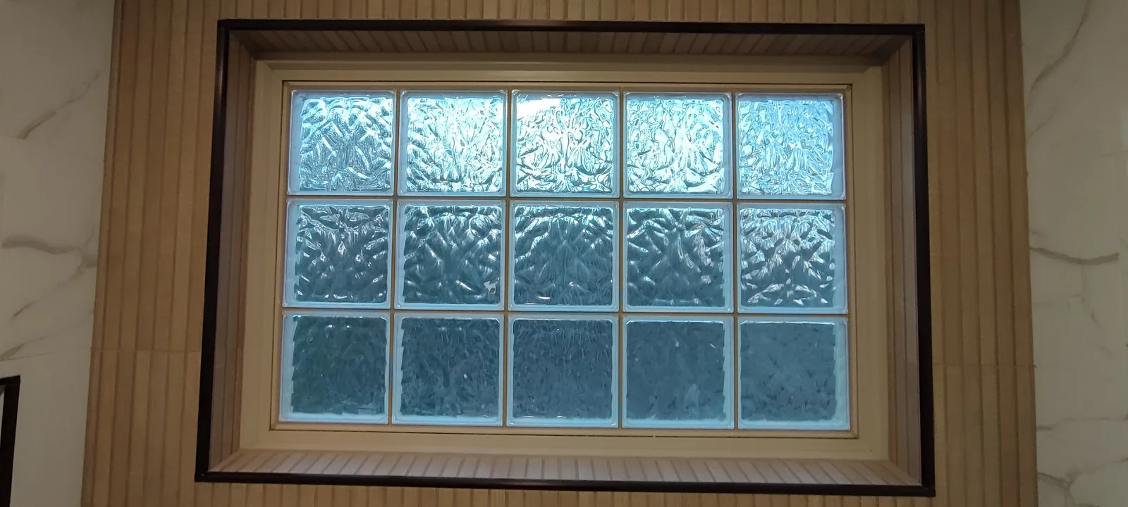 Glass-block window framed by wood-look tiles, photographed at the tile completion stage.