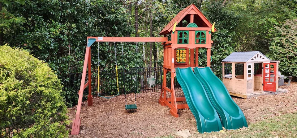 Completed wooden playset with play tower, slide and swings in a backyard.